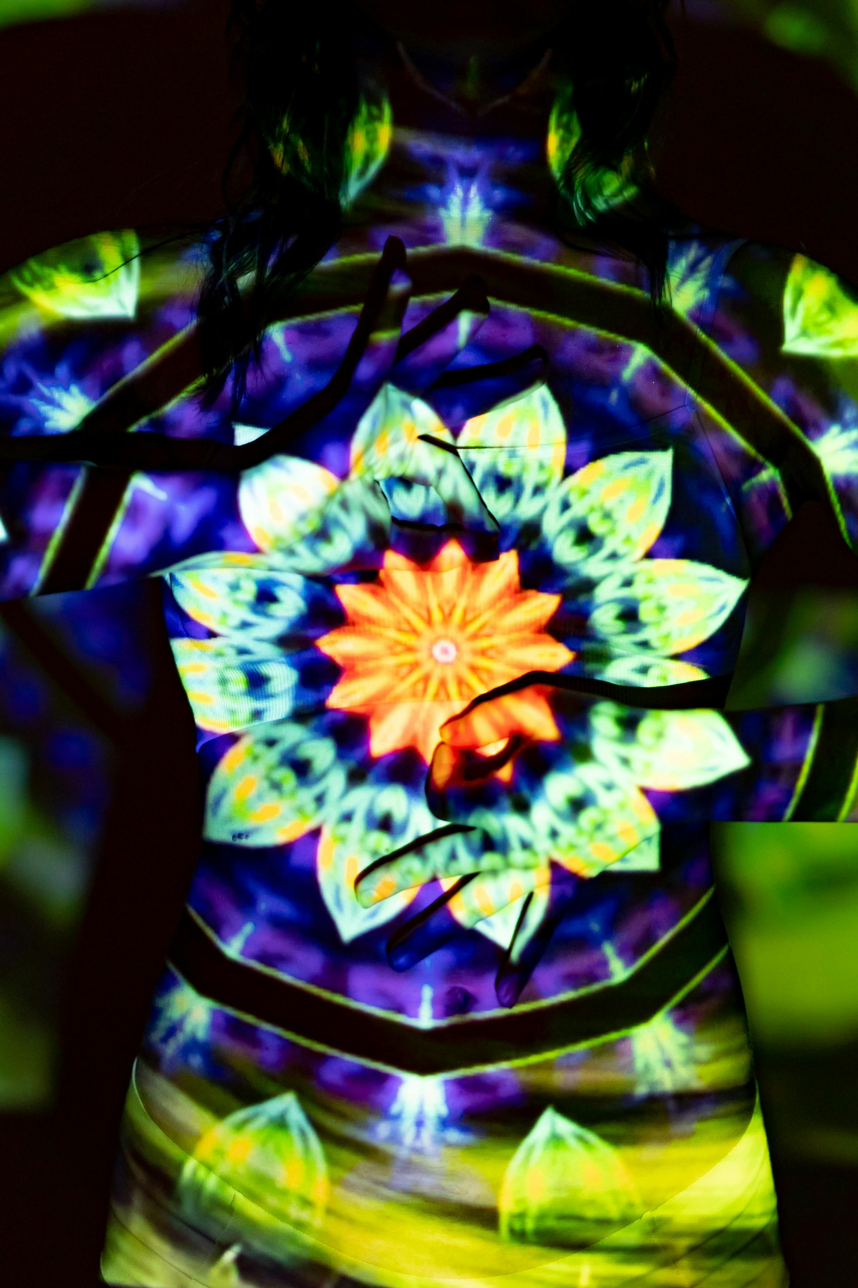A dynamic and colorful kaleidoscopic mandala art projected onto a woman's silhouette, creating a surreal visual effect.